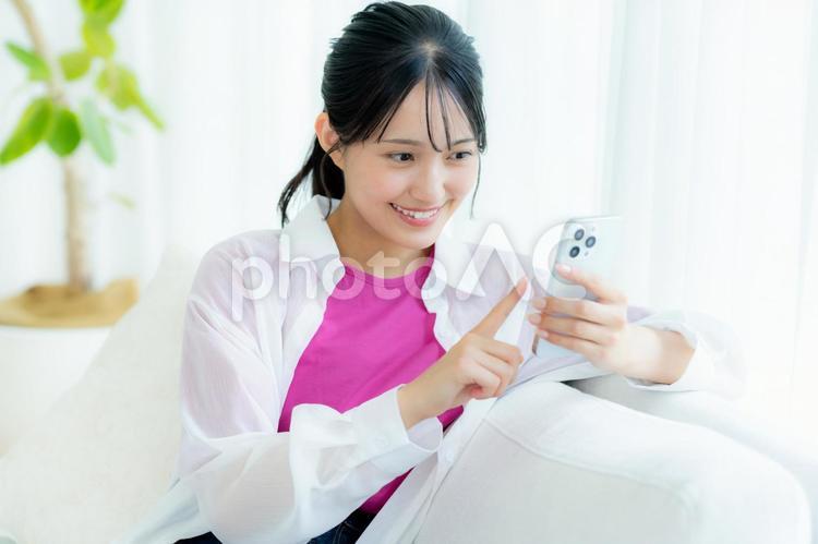 部屋でスマホを操作する若い女性 スマホ,笑顔,女性の写真素材