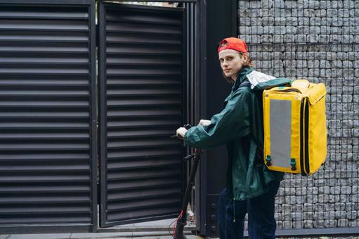 電動キックボードで配達に来たカメラ目線の男性 配達,フードデリバリー,デリバリーの写真素材