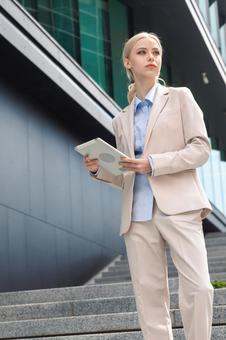 オフィスビルの外の階段でタブレットを持って遠くを見ているビジネスウーマン ビジネスウーマン,ビジネス,女性の写真素材