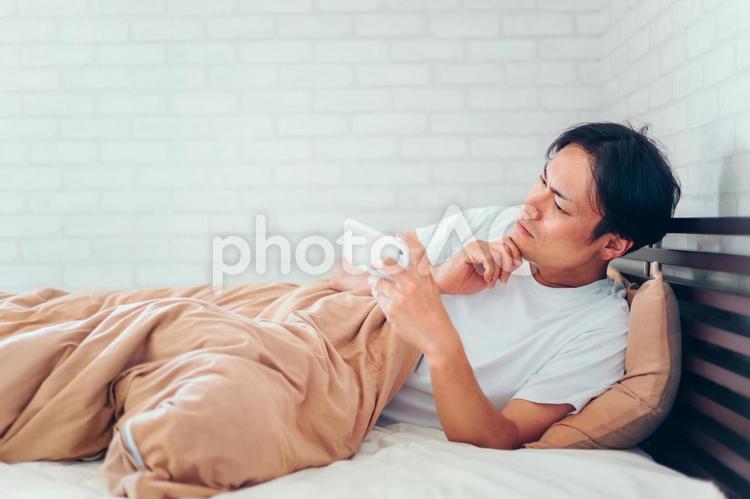 ベッドで寝ながらスマホを見る男性 ベッド,スマホ,寝る前スマホの写真素材