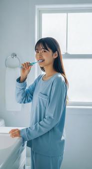 朝の洗面所で歯磨きをする若い女性 朝の洗面所で歯磨きをする若い女性の写真