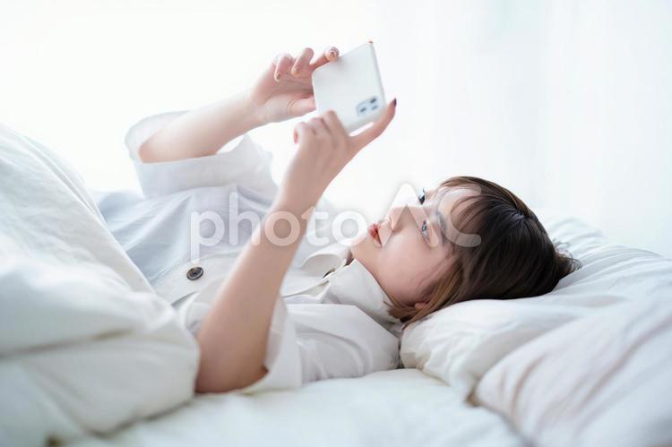 ベッドの上でスマートフォンを操作する女性  女性,スマートフォン,昼の写真素材
