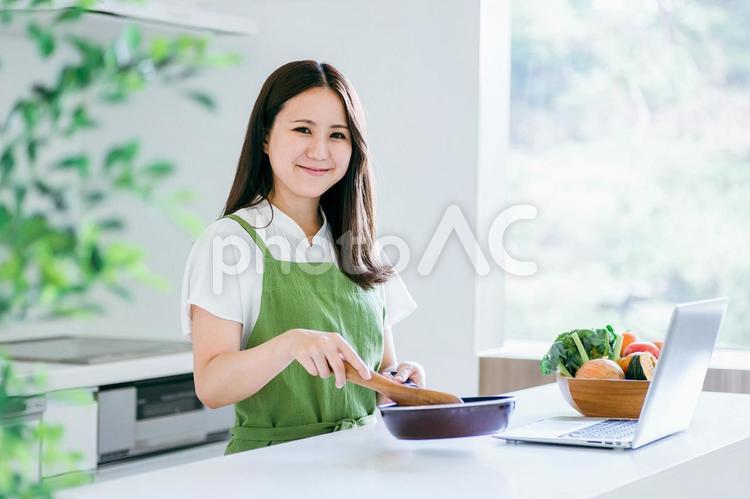 パソコンを見ながら料理する女性（笑顔） 料理,家事,パソコンの写真素材