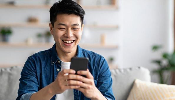 スマホで笑顔を見せる若い男性の室内シーン スマホで笑顔を見せる若い男性の室内シーンの写真
