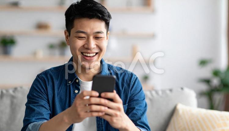 スマホで笑顔を見せる若い男性の室内シーン 人物,男性,20代の写真素材