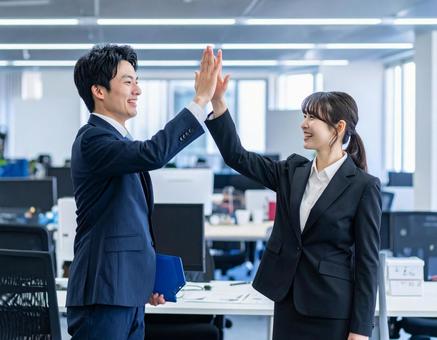 職場でハイタッチして喜ぶ男性と女性 職場でハイタッチして喜ぶ男性と女性の写真