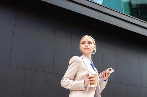 オフィスビルの外でコーヒーとスマートフォンを持って立っているビジネスウーマン ビジネスウーマン,ビジネス,女性の写真素材