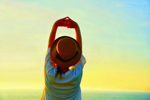 夕焼け空を見ながらリラックスする女性 夕焼け空を見ながらリラックスする女性 女性,夕日,海の写真素材