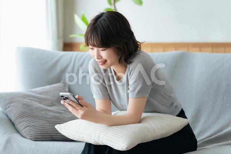 ソファに座ってスマホを使う笑顔の女性 女性,スマホ,スマートフォンの写真素材