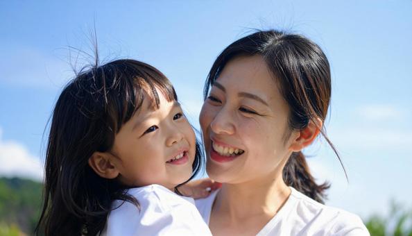 青空の下、子供を抱っこする母親 青空の下、子供を抱っこする母親の写真