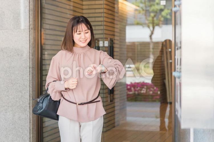 腕時計を見ながらビルから出てくる女性 通勤,出勤,女性の写真素材