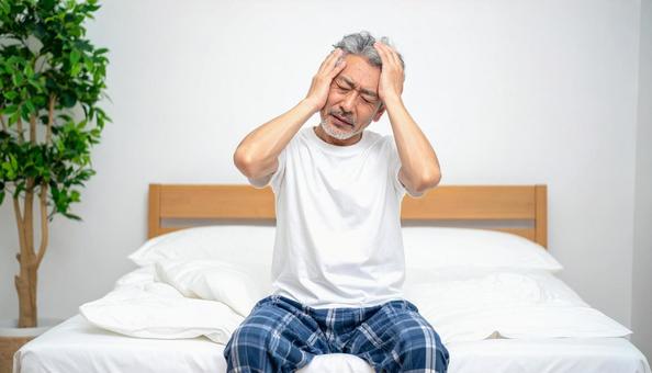 寝起きで座って頭を抱えるパジャマ姿の男性 寝起きで座って頭を抱えるパジャマ姿の男性の写真