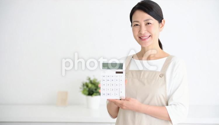 電卓を持つミドル日本人女性の主婦 電卓,エプロン姿,カメラ目線の写真素材