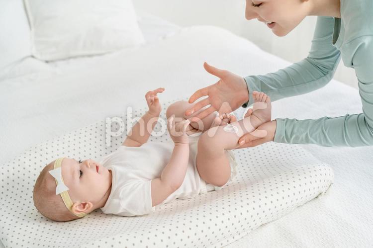 笑顔で仰向けの赤ちゃんの足にクリームを塗る女性 赤ちゃん,仰向け,足の写真素材