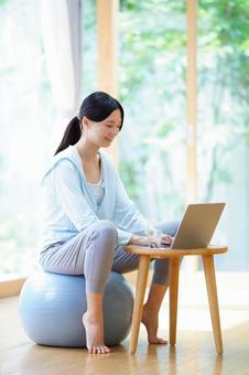 つま先立ちでボールに座りパソコンをする女性 女性,バランスボール,ノートパソコンの写真素材