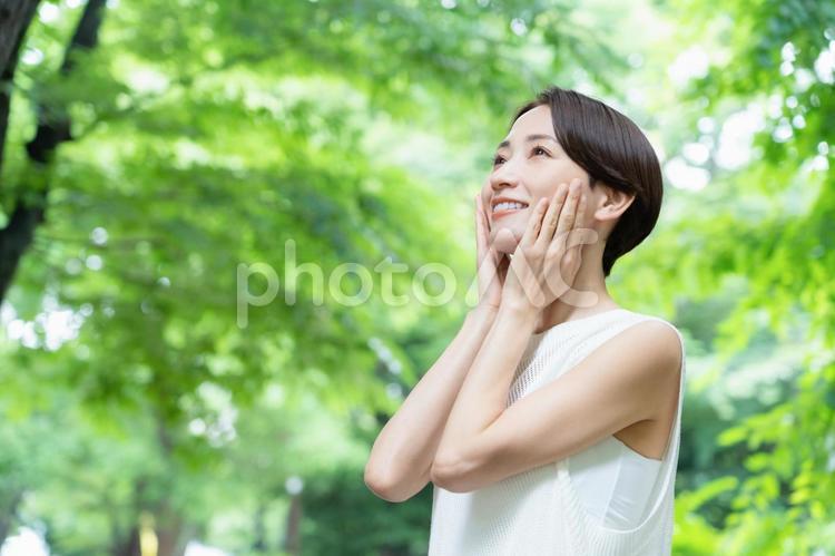 新緑の中でスキンケアをするミドルの女性 ビューティー,女性,スキンケアの写真素材