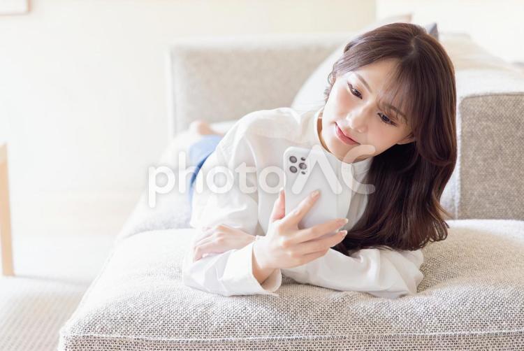 ソファーに寝転びスマホで検索する女性 女性,検索,スマートフォンの写真素材