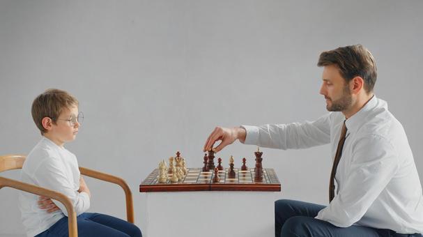 向かい合いチェスをしているお父さんと男の子(グレー背景) 向かい合いチェスをしているお父さんと男の子(グレー背景) チェス,親子,お父さんの写真素材