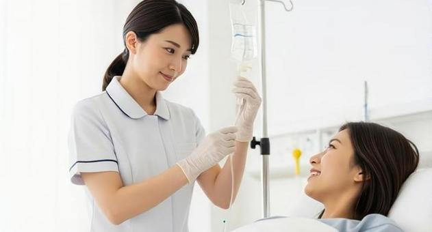 患者の点滴を調整するアジア人看護師 患者の点滴を調整するアジア人看護師の写真