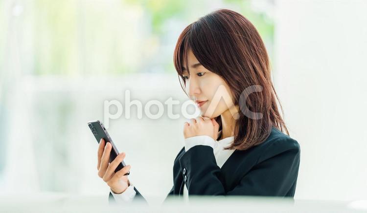 スマホの画面を見て考えるビジネスウーマン 女性,ビジネス,スマホの写真素材