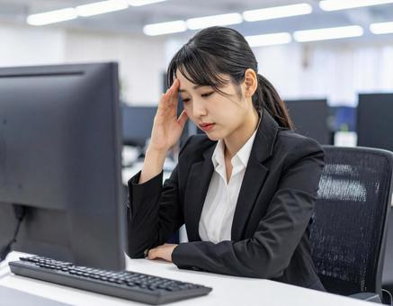 パソコンの前で頭を抱える女性 パソコンの前で頭を抱える女性の写真