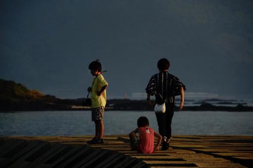<素材>夕方の防波堤で海を眺める親子 <素材>夕方の防波堤で海を眺める親子の写真