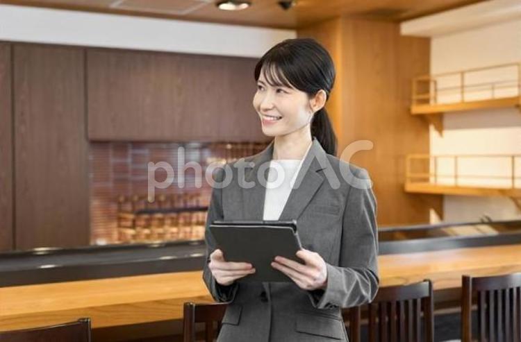 タブレットを持って店内を見る女性 飲食店,女性,スーツの写真素材