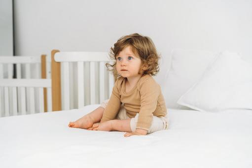 ベッドに1人で座るくせ毛の子供 ベッドに1人で座るくせ毛の子供 赤ちゃん,かわいい,お座りの写真素材