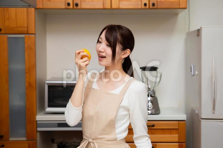 キッチンでレモンをかじろうとしている笑顔の若い日本人女性 キッチン,台所,レモンの写真素材