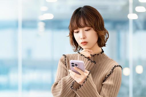 スマホを見て考える女性・ビジネスウーマン スマホを見て考える女性・ビジネスウーマン 女性,困る,考えるの写真素材