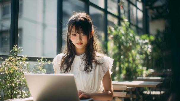 緑豊かなカフェでノートPCを使用する女性 緑豊かなカフェでノートPCを使用する女性の写真