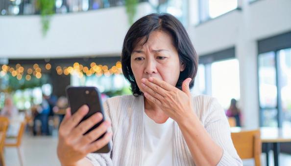 カフェでスマホを見てショックを受ける女性の写真