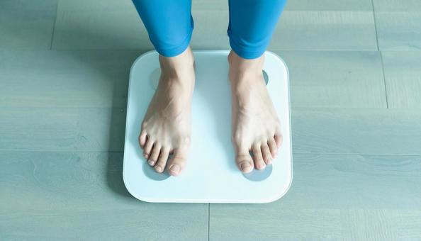 白い体重計に足を乗せる若い女性 白い体重計に足を乗せる若い女性の写真