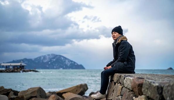 冬の空の下、一人旅を楽しみ石垣に座る男性 冬の空の下、一人旅を楽しみ石垣に座る男性の写真