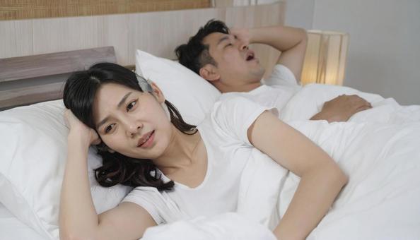 ベッドで夫のいびきで睡眠不足の妻 ベッドで夫のいびきで睡眠不足の妻の写真