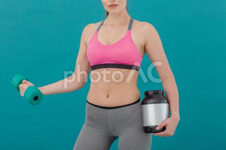 プロテインを持ちながらダンベル運動する女性（緑背景） シェイプアップ,ダイエット,女性の写真素材