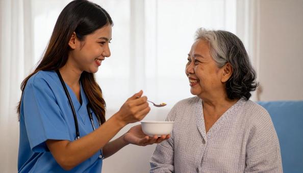 ゼリーをシニア女性に食べさせる介護士の写真