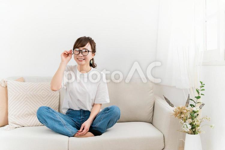家のソファに座るデニム姿のおしゃれな女性 メガネ,眼鏡,女性の写真素材