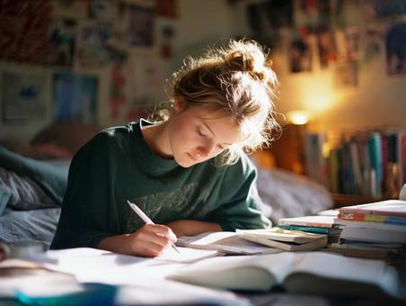 本に囲まれ、集中して書き物をする若い女性 本に囲まれ、集中して書き物をする若い女性の写真