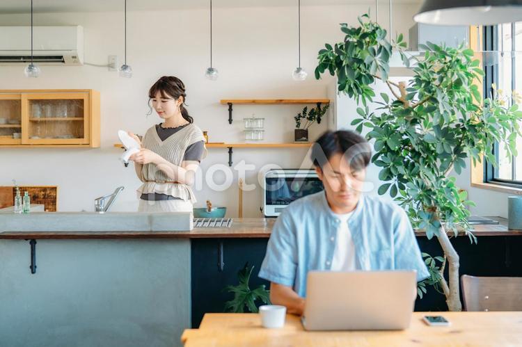 テレワークする男性とキッチンにいる女性（笑顔） テレワーク,パソコン,夫婦の写真素材