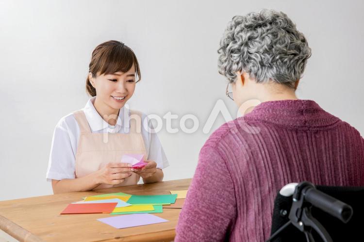 折り紙でレクリエーションする介護士と高齢者の女性 老人ホーム,折り鶴,レクリエーションの写真素材