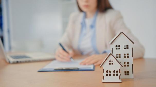 家と車の模型を置いて仕事をする女性スタッフ 保険業,事務職,接客業の写真素材