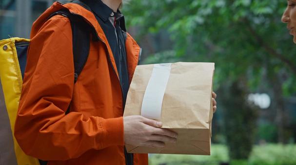 街なかで紙袋を持って立つフードデリバリーの男性 配達,フードデリバリー,デリバリーの写真素材