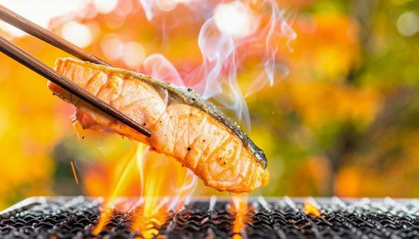 七輪で焼いている焼き鮭を箸でとるの写真