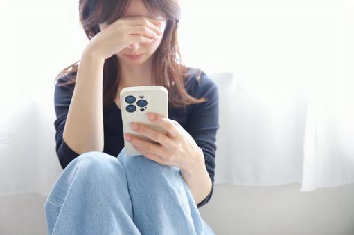 スマートフォンを見て落ち込む女性 スマートフォンを見て落ち込む女性 スマホ,落ち込む,悩みの写真素材