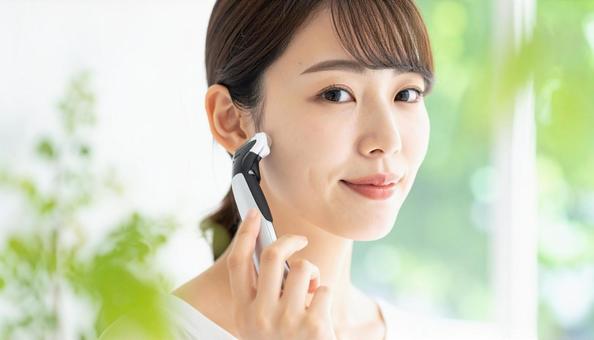 電気シェーバーで顔剃りする若い日本人女性の写真