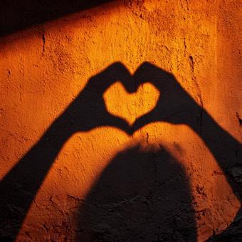 オレンジの壁に映る手で作ったハートの影の写真
