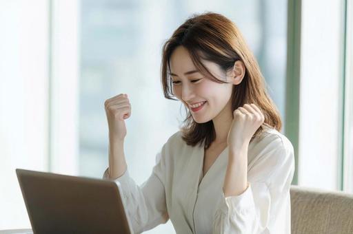 PC前で笑顔のガッツポーズ女性 PC前で笑顔のガッツポーズ女性の写真