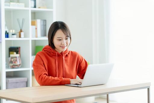 リビングでパソコンを使う若い女性 リビングでパソコンを使う若い女性の写真