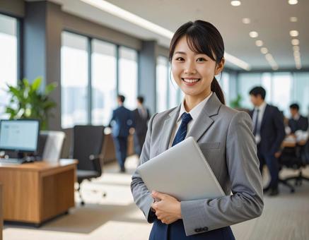 オフィスでPCを持って微笑む女性社員 オフィスでPCを持って微笑む女性社員の写真